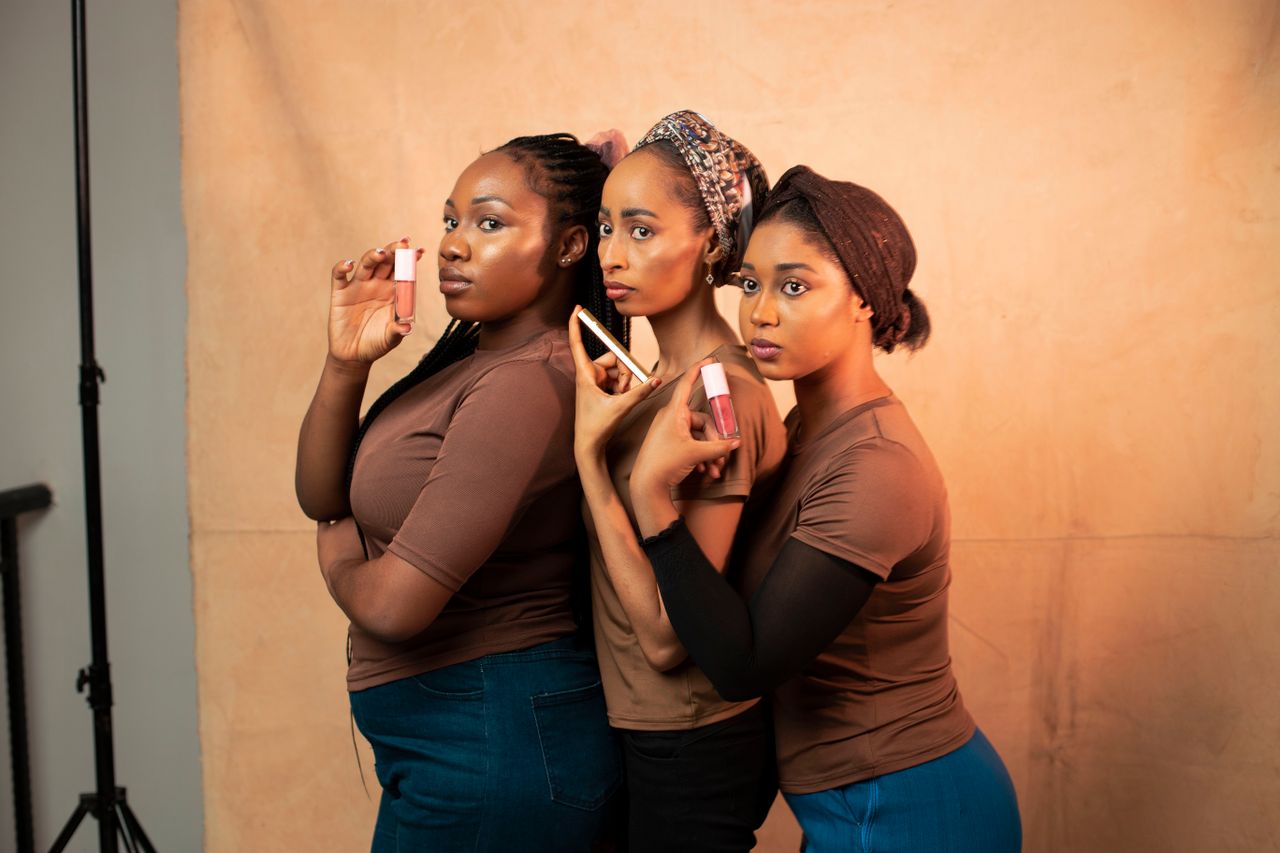 Three women presenting lipstick products with confidence on a neutral backdrop.