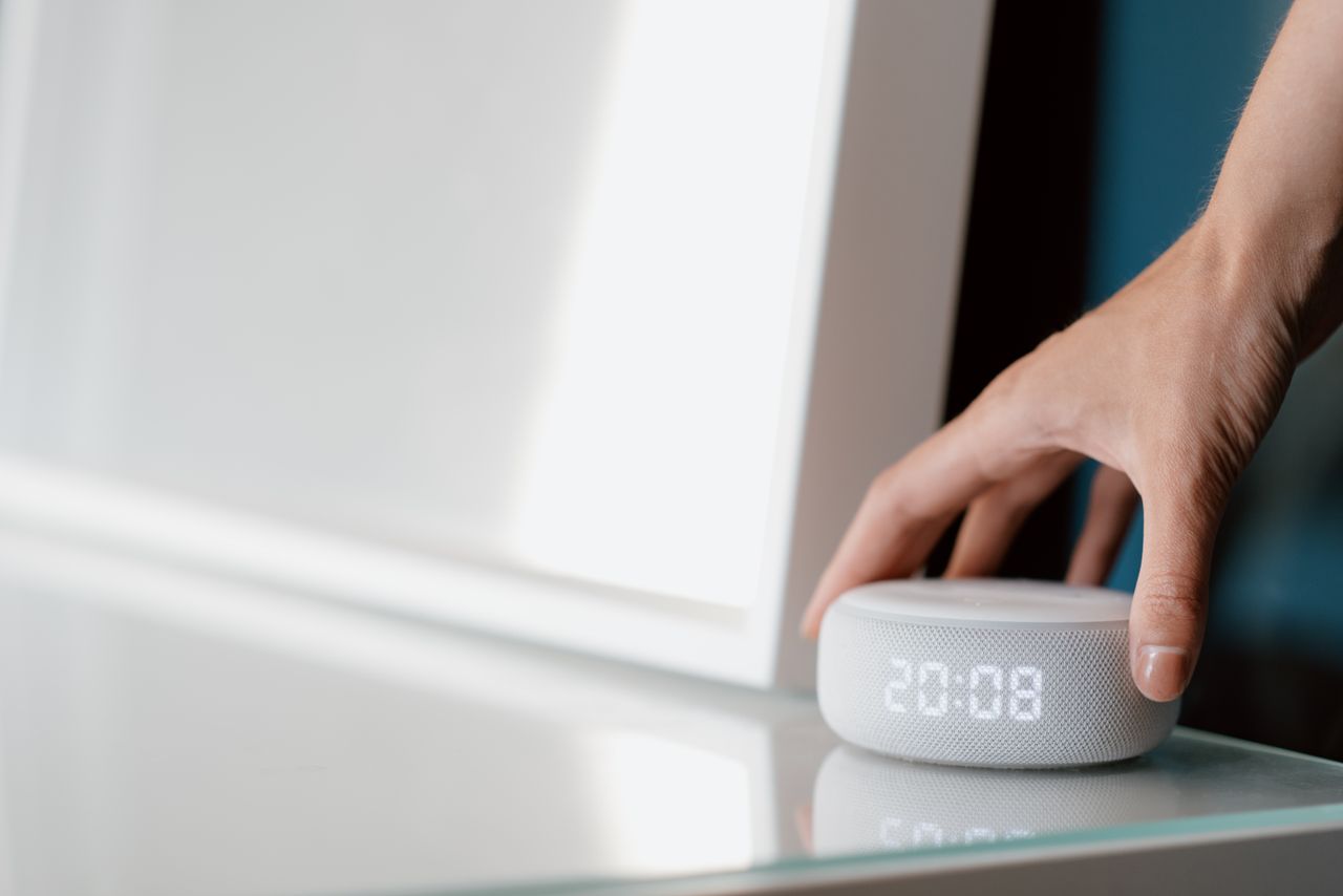 Mastering the First Impression: Your intriguing post title goes here Close-up of a hand adjusting a smart speaker displaying time indoors.